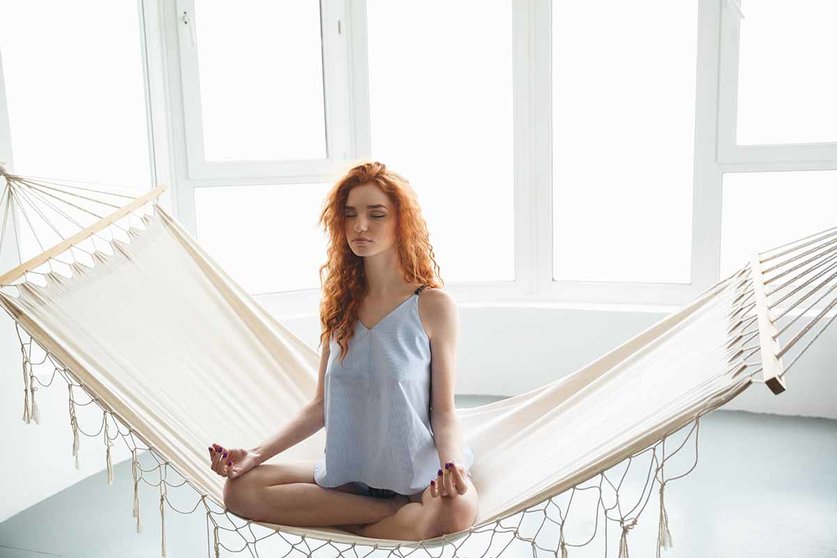 Image of cute concentrated young redhead lady sitting on hammock meditate. Eyes closed.